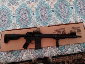 Black rifle on cardboard box atop bed